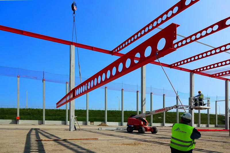 Lochner-Monteure beim Einheben eines roten Stahlträgers mit Kran und Arbeitsbühne